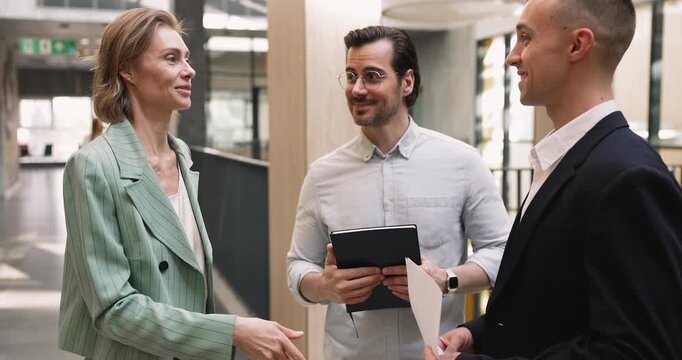 Businesswoman talking during meeting with male colleagues standing in office hallway, shaking hands, expressing appreciation for successful teamwork, good work results. Partnership, business relations