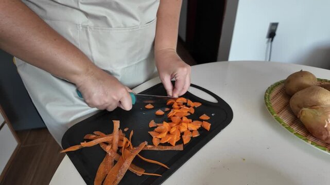 A woman cuts peeled carrots with a sharp knife on a cutting board