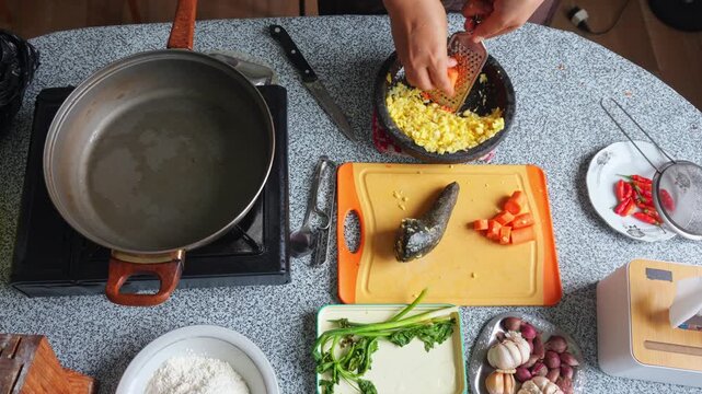 Top-down view of Hands grating fresh carrots into stone bowl filled with corn kernels for fritters
