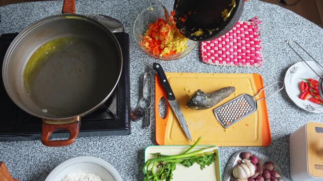 Top view of hands adding spices to bowl of corn and vegetable fritter batter on busy kitchen counter
