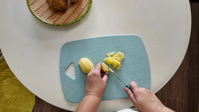 Woman standing at the kitchen table cuts potatoes for lunch with a sharp knife