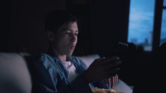 Evening Calm: Boy in Solitude by the Window, Enjoying Chips and Engaged with His Phone