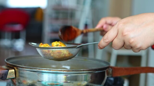 Close-up of hands home chef lifting golden-brown corn fritters from hot oil with mesh strainer and wooden spoon
