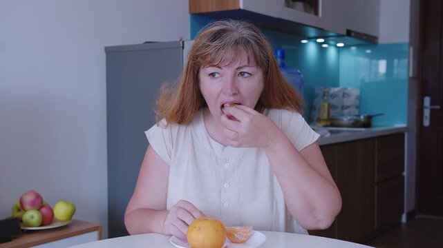 Woman who sits at a table and divides a tangerine into slices