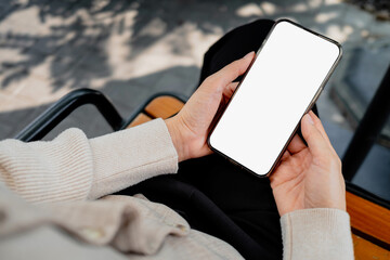Close-up of hands holding a blank smartphone screen outdoors on a wooden bench, ideal for app mockups, mobile UI design, advertising, and digital marketing concepts.