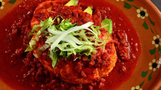 Mexican cuisine, spicy stuffed bread dipped in red pepper sauce, lettuce and avocado on top, pambazo