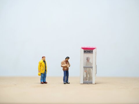 Mini toy of action figure at table with blurred background. Miniature photography concept design. Minifigure of worker character with atm box.