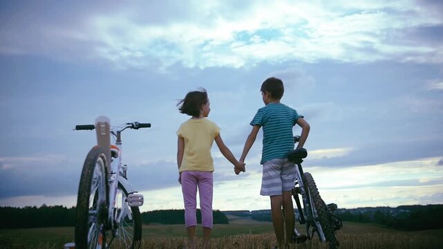 Sunset Joy: Kids Enjoying a Heartwarming Hug After an Energetic Bike Ride in the Open Field