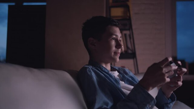 Young Boy Sitting on the Couch at Night, Emotionally Immersed in Playing Video Games at Home