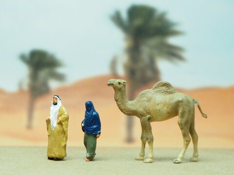 Mini toy of action figure with blurred background. Miniature photography concept design. Minifigure of arabian people and camel character at desert.