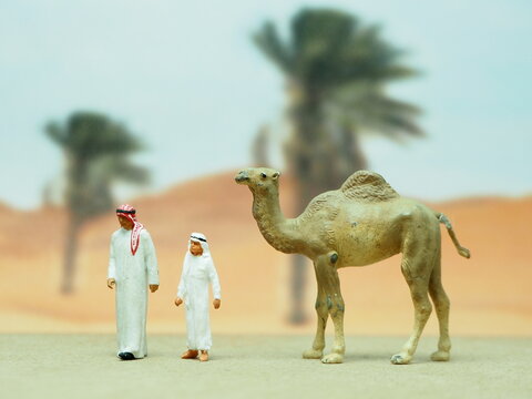 Mini toy of action figure with blurred background. Miniature photography concept design. Minifigure of arabian people and camel character at desert.