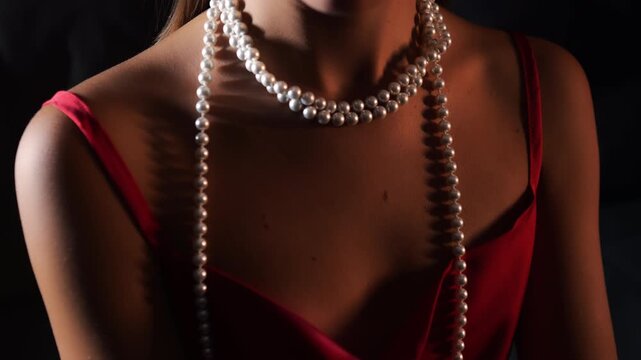 Close up of elegant woman wearing red dress and pearl necklace in dramatic light. Luxury fashion concept, sensual style and classic jewelry indoors.