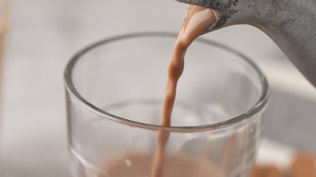 Indian chai served in glass cups, brewed in a metal kettle with aromatic masalas. Getting poured on glass.