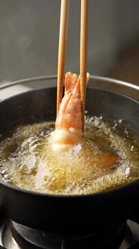 Delicious shrimp tempura, expertly lowered by chopsticks, begins frying in golden bubbling oil. Savory seafood cooking ensures crispy culinary experience