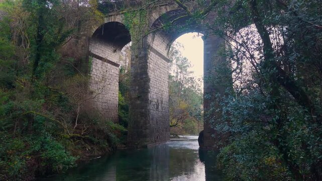 San Crimenzo River With Arches Of Ponte Peon - Stone Viaduct Bridge In Dumbria, Spain. pullback drone shot