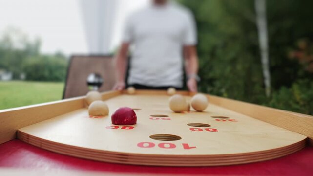 Close up of wooden tabletop shuffleboard style game with player in background. Outdoor leisure activity, summer backyard entertainment and casual competition.