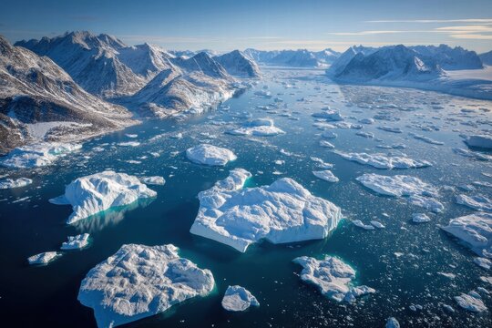 Vista a&eacute;rea de icebergs flutuando em &aacute;guas geladas cercadas por montanhas nevadas na Groenl&acirc;ndia durante um dia ensolarado de inverno.