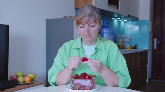 Portrait of a woman eating ripe strawberries, sitting at a table
