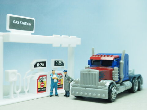 Mini toy of action figure at table with blurred background. Toy photography concept design. Heavy truck at gas station. Filling fuel at public gas station.
