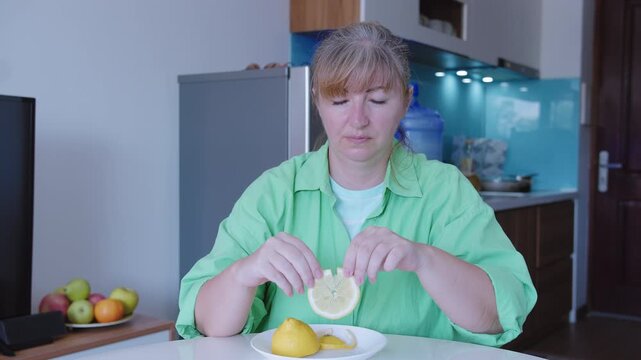 A woman eats a sour lemon, sitting at a table
