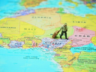 Naklejka premium Mini toy of action figure at paper book with blurred bacground. Miniature photography concept design. Minifigure of people traveling at Africa country continent with maps.