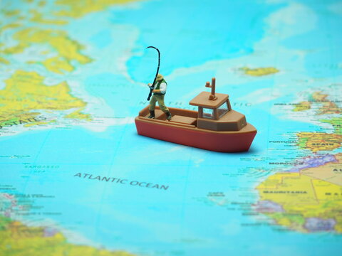 Mini toy of action figure at paper book with blurred bacground. Miniature photography concept design. Minifigure of professional fisherman fishing at Atlantic Ocean with tugboat.