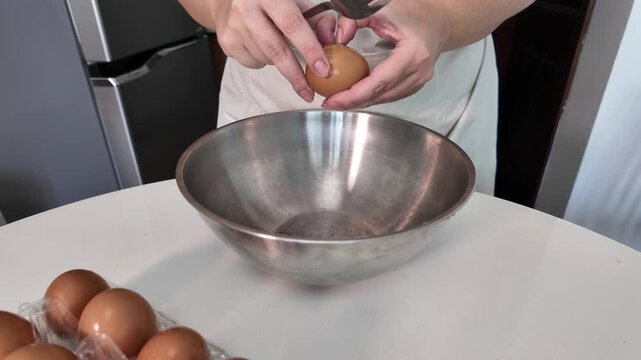 Female hands break an egg with a knife. A woman breaks an egg into a metal bowl.