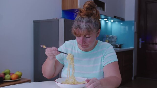 Woman eats Asian noodles with chopsticks. A woman eats street food at home, at the kitchen table.