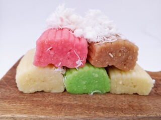 Close up of colorful Indonesian steamed cassava cakes topped with freshly grated coconut, beautifully stacked and served on a rustic wooden board