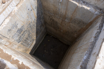 Looking down into deep, dark, mysterious concrete hole. An empty, old well or abandoned pit with grunge texture, evoking sense of mystery and confinement