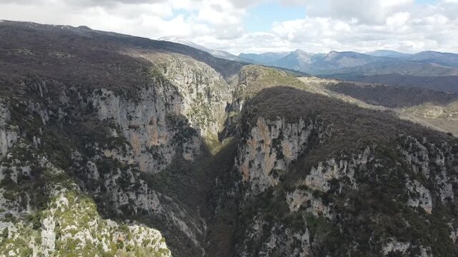A cinematic wide drone shot capturing the immense scale of Vikos Gorge. Highlighting the towering limestone cliffs and the rugged wilderness of the Pindus Mountains in Northern Greece.