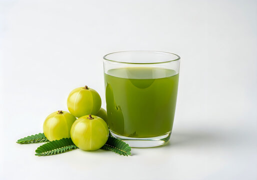 A glass of green juice with amla fruits and leaves on white background