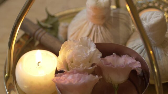 Close-up view of traditional white herbal compress balls on a tray prepared for Ayurvedic massage therapy. Relaxing spa atmosphere with warm lighting and pinda sweda tools for body treatment.
