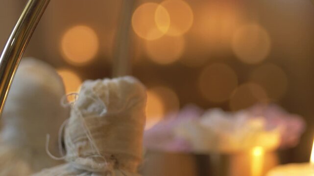 Traditional white herbal compress balls on a tray prepared for Ayurvedic massage therapy. Relaxing spa atmosphere with warm lighting and pinda sweda tools for body treatment.