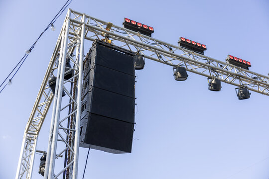 Outdoor concert stage with professional audio sound system speakers and lights hanging on metal truss structure, evoking feeling of powerful anticipation for show