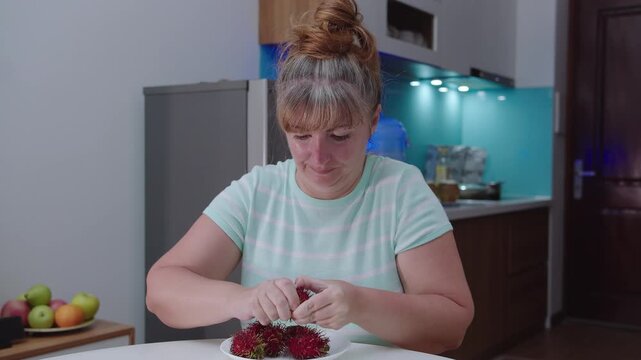 A woman peels and eats rambutan, sits at home