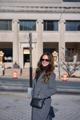 Fototapeta premium Smiling woman in sunglasses wearing gray coat on city street in winter
