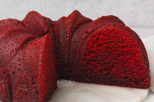 closeup view of cross-section of a red velvet bundt cake on marble cake plate, red velvet cake slice on on a white countertop, red bundt cake slice on a white granite background