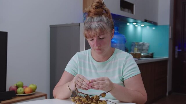 Portrait of a woman eating an exotic longan fruit on the background of a kitchen.
