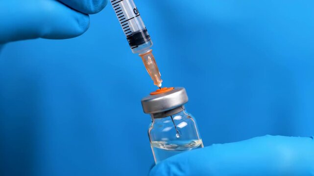 Vaccine preparation close up as doctor hands in blue medical gloves use a syringe to extract liquid medicine from a glass vial for patient immunization and virus prevention