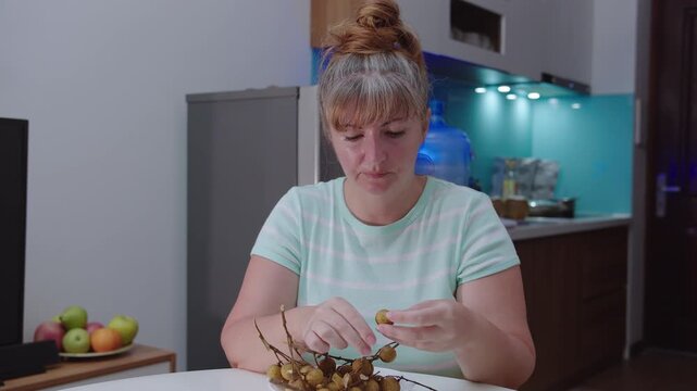 Woman eating an exotic longan fruit on the background of a kitchen.