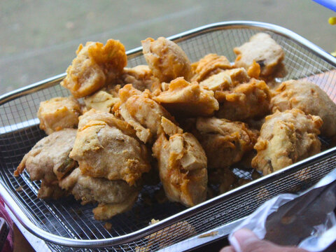 Fried tofu snacks in metal wire basket at local market. Traditional Asian street food preparation in outdoor environment representing authentic culinary culture and fast food lifestyle.