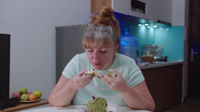 Close-up of a woman eating a sugar apple in the background of a kitchen.