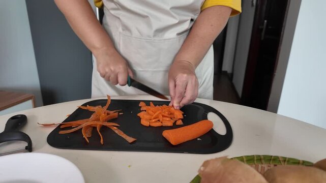 Hands of a woman standing at the table, peeling carrots with a vegetable peeler