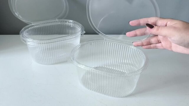 A woman's hand touches a plastic disposable transparent food container on the table. Takeaway. The danger of micropalstick in food