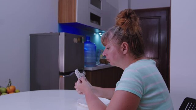 A woman sits at a table, kitchen background and eats a dragon fruit