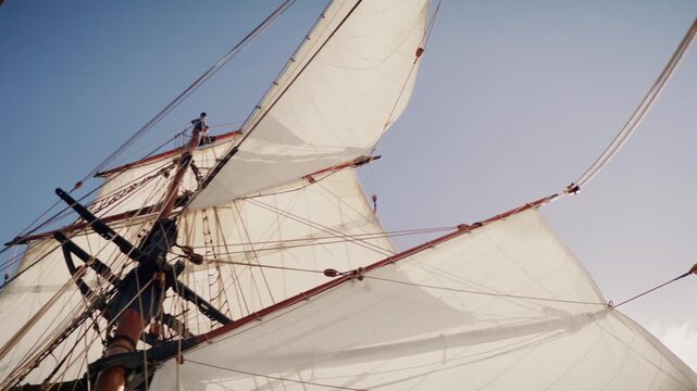 Upward view of tall ship sails and rigging against blue sky in sunlight