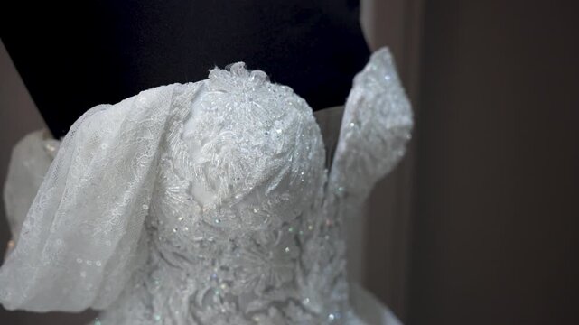 Close-up view shows intricate lace and beadwork on a wedding dress. The setting is a bridal shop during early afternoon light. Focus on the craftsmanship and design elements.