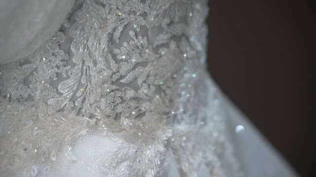 Close-up view shows intricate lace and beadwork on a wedding dress. The setting is a bridal shop during early afternoon light. Focus on the craftsmanship and design elements.