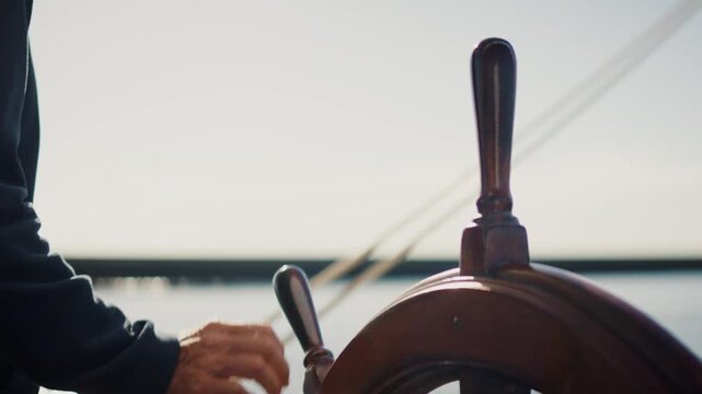 Hand steering wooden ship wheel on traditional sailing vessel under sunlight